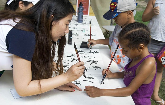 A volunteer teaches a young visitor how to write Chinese characters at the 2014 Folklife Festival. Photo by Bea Ugolini, Ralph Rinzler Folklife Archives and Collections, Smithsonian Institution